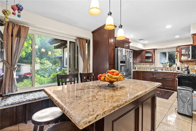 kitchen featuring light stone countertops, decorative light fixtures, decorative backsplash, light tile patterned floors, and appliances with stainless steel finishes