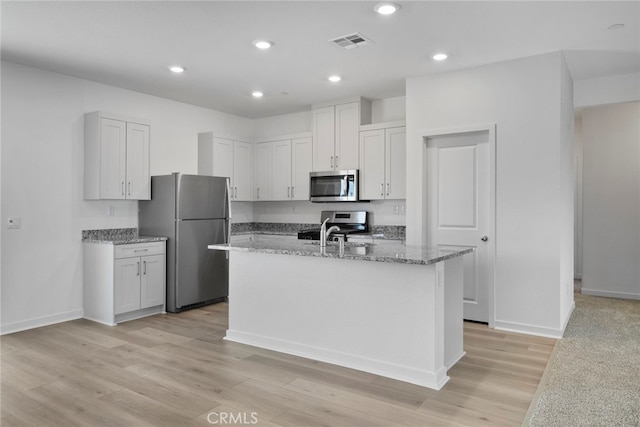 kitchen with appliances with stainless steel finishes, light wood-type flooring, light stone counters, white cabinets, and an island with sink