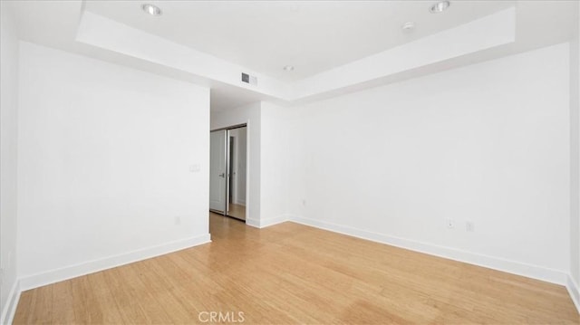 empty room featuring a raised ceiling and light hardwood / wood-style flooring