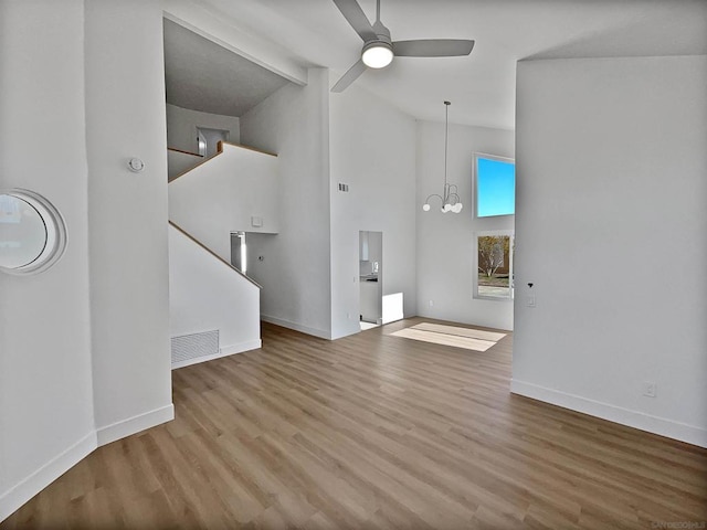 unfurnished living room with ceiling fan with notable chandelier, beam ceiling, and hardwood / wood-style floors