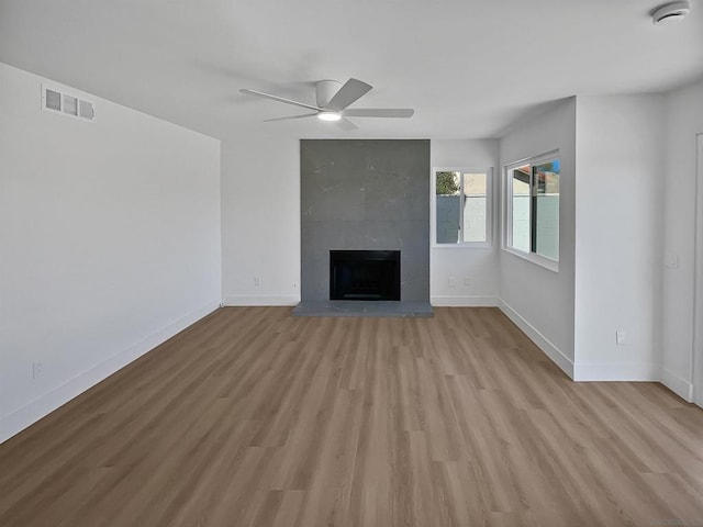 unfurnished living room with a tiled fireplace, ceiling fan, and light hardwood / wood-style flooring