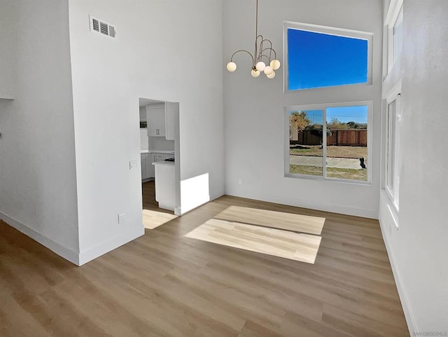 unfurnished dining area with a notable chandelier, light hardwood / wood-style floors, and a high ceiling