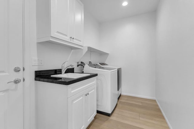 clothes washing area with light hardwood / wood-style floors, cabinets, independent washer and dryer, and sink