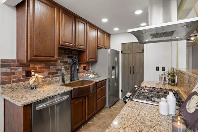 kitchen with tasteful backsplash, light stone counters, island range hood, stainless steel appliances, and sink