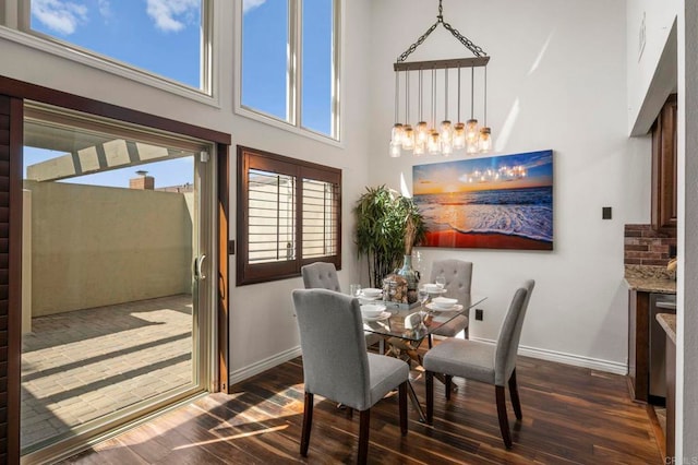 dining space featuring dark hardwood / wood-style flooring, a towering ceiling, and an inviting chandelier