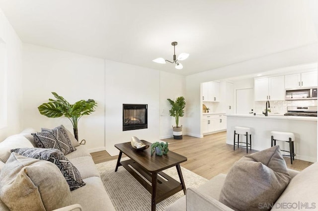 living room with light wood-type flooring, sink, and an inviting chandelier