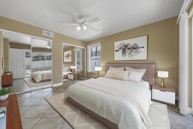 bedroom featuring ceiling fan, light tile patterned floors, and multiple closets