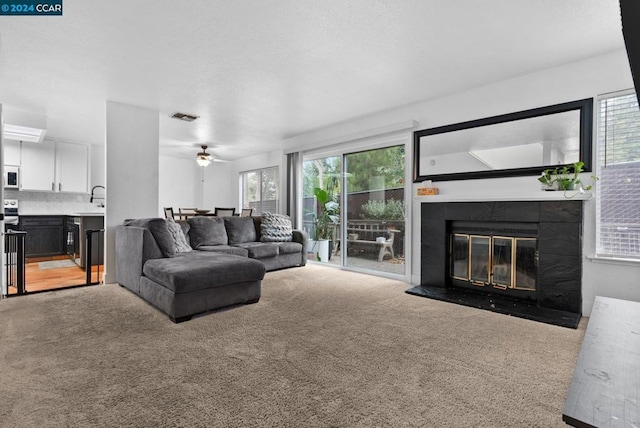 carpeted living room featuring sink, ceiling fan, and a tiled fireplace