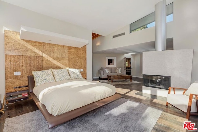 bedroom with a multi sided fireplace, high vaulted ceiling, and wood-type flooring