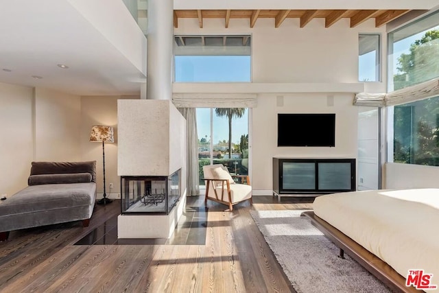 bedroom with a multi sided fireplace, wood-type flooring, and beamed ceiling