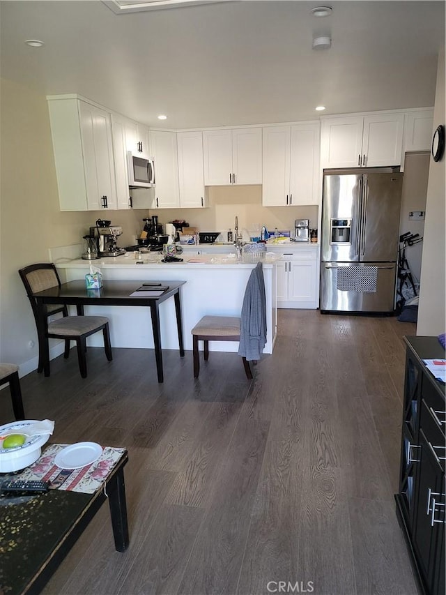 kitchen featuring a kitchen breakfast bar, white cabinetry, dark hardwood / wood-style flooring, and appliances with stainless steel finishes