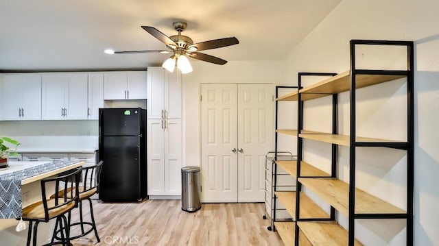 kitchen featuring white cabinets, light wood-type flooring, black fridge, and ceiling fan