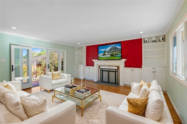 living room with built in shelves, light hardwood / wood-style floors, crown molding, and french doors