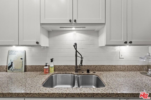 kitchen with white cabinets, sink, light stone countertops, and backsplash