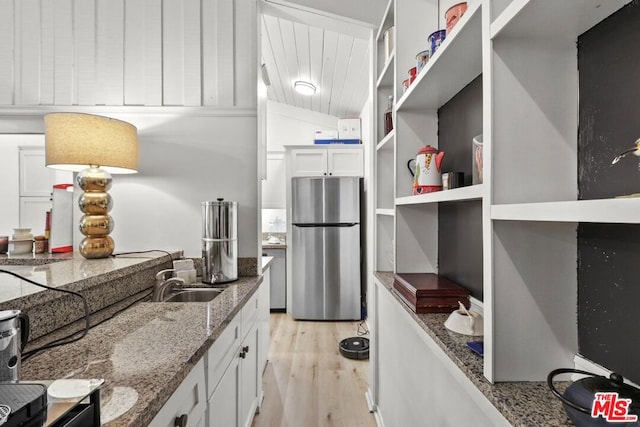 kitchen with stone countertops, stainless steel fridge, white cabinetry, and sink