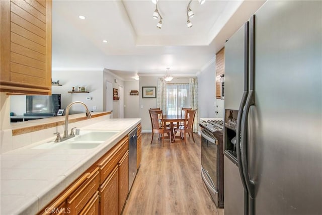 kitchen featuring stainless steel appliances, sink, tile countertops, light hardwood / wood-style floors, and hanging light fixtures