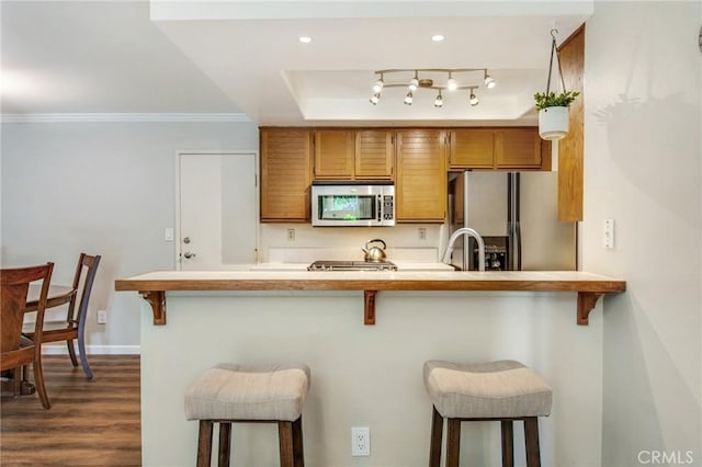 kitchen featuring a kitchen breakfast bar, dark hardwood / wood-style floors, ornamental molding, kitchen peninsula, and stainless steel appliances