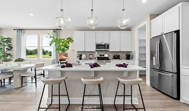 kitchen featuring pendant lighting, white cabinets, a kitchen island with sink, and appliances with stainless steel finishes