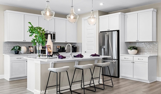 kitchen with white cabinets, light wood-type flooring, an island with sink, and appliances with stainless steel finishes