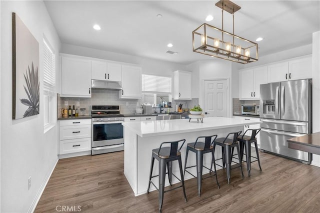 kitchen featuring dark wood-type flooring, white cabinets, pendant lighting, a kitchen island, and appliances with stainless steel finishes