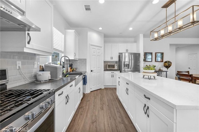 kitchen with dark hardwood / wood-style flooring, stainless steel appliances, pendant lighting, white cabinets, and range hood