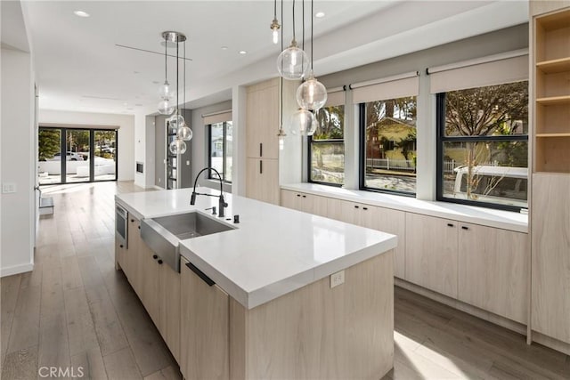 kitchen featuring light brown cabinets, a kitchen island with sink, sink, light hardwood / wood-style flooring, and decorative light fixtures