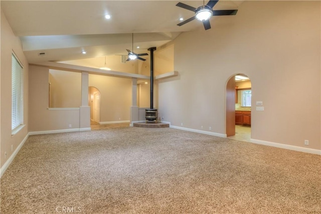 unfurnished living room with a wood stove, high vaulted ceiling, ceiling fan, and light carpet