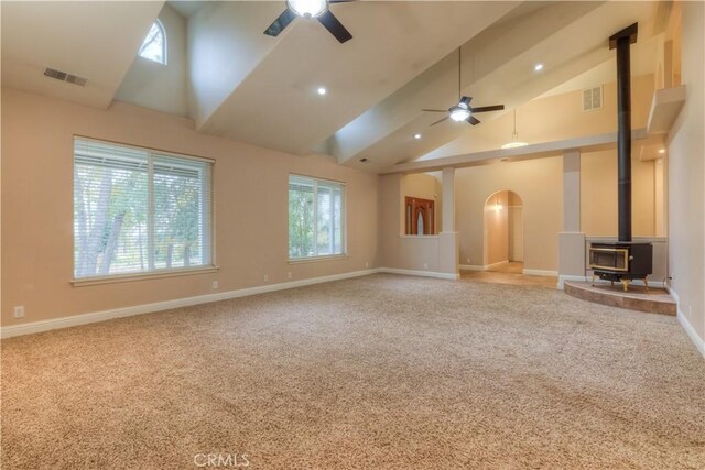 unfurnished living room featuring a wood stove, ceiling fan, light carpet, and a healthy amount of sunlight