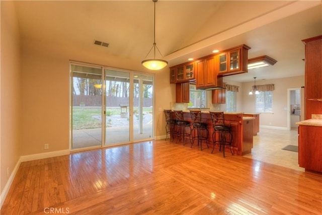 kitchen featuring decorative light fixtures, a kitchen bar, kitchen peninsula, and light wood-type flooring