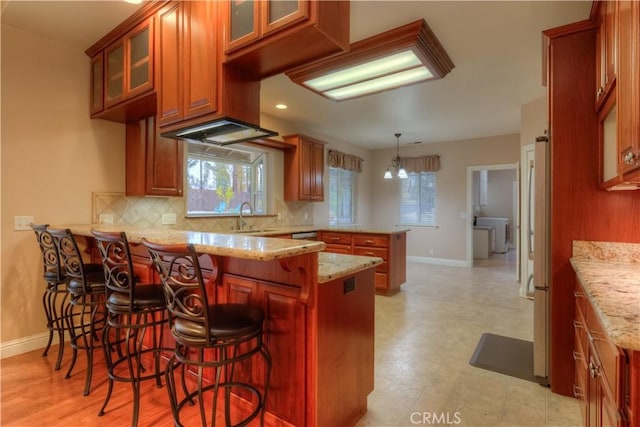 kitchen featuring a kitchen bar, decorative light fixtures, kitchen peninsula, a chandelier, and light stone counters