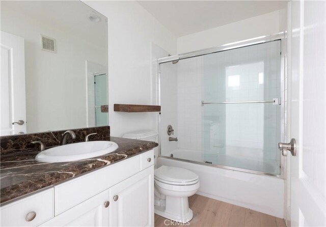 full bathroom featuring hardwood / wood-style floors, vanity, toilet, and bath / shower combo with glass door