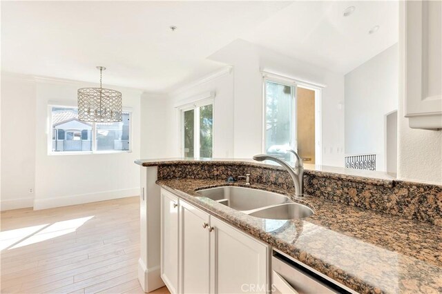 kitchen with a wealth of natural light, dark stone counters, sink, decorative light fixtures, and white cabinetry