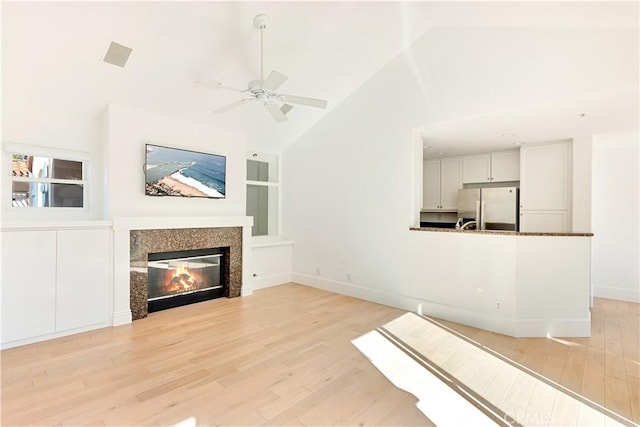 unfurnished living room featuring ceiling fan, light wood-type flooring, high vaulted ceiling, and a tiled fireplace