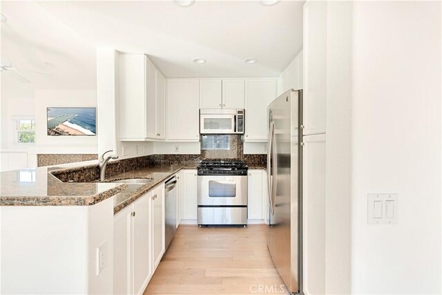 kitchen featuring kitchen peninsula, white cabinets, dark stone counters, and appliances with stainless steel finishes