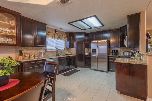 kitchen with a textured ceiling, appliances with stainless steel finishes, tasteful backsplash, light stone counters, and dark brown cabinetry