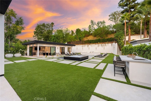 back house at dusk featuring a yard, a water view, area for grilling, and an outdoor wet bar