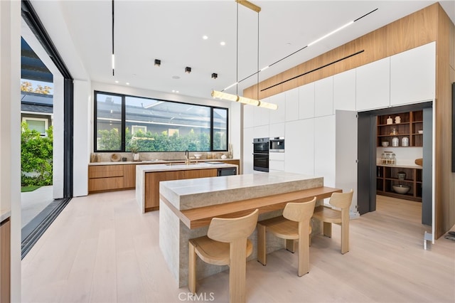 kitchen with pendant lighting, white cabinets, sink, light hardwood / wood-style flooring, and a kitchen island