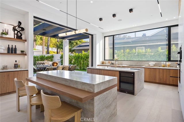 kitchen featuring beverage cooler, sink, light hardwood / wood-style flooring, a center island, and hanging light fixtures