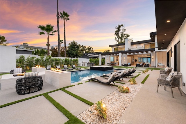 pool at dusk featuring a patio and an outdoor living space with a fire pit