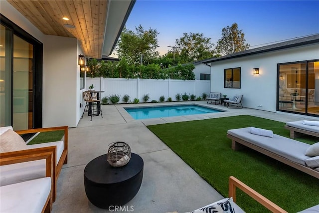 pool at dusk with a lawn, a patio, and an outdoor hangout area