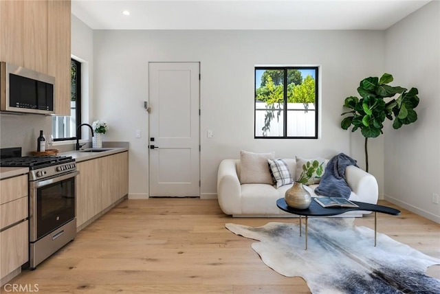 kitchen with sink, light brown cabinetry, light wood-type flooring, and appliances with stainless steel finishes