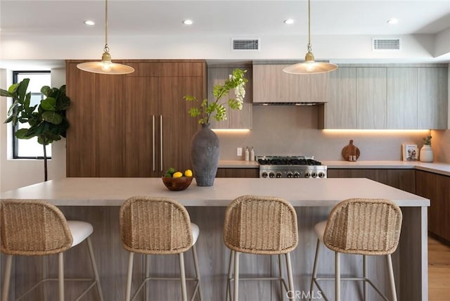 kitchen featuring a breakfast bar, stainless steel range, decorative light fixtures, and light hardwood / wood-style flooring