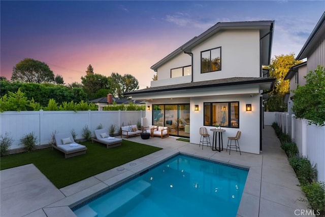 back house at dusk with a fenced in pool, outdoor lounge area, a patio area, and a bar