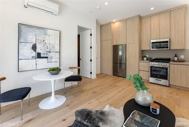 kitchen with an AC wall unit, light brown cabinets, light hardwood / wood-style flooring, and appliances with stainless steel finishes