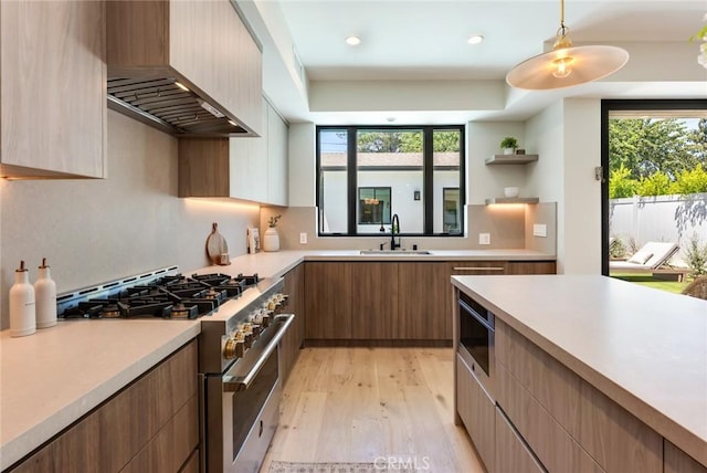 kitchen featuring sink, hanging light fixtures, wall chimney range hood, light hardwood / wood-style floors, and high end range