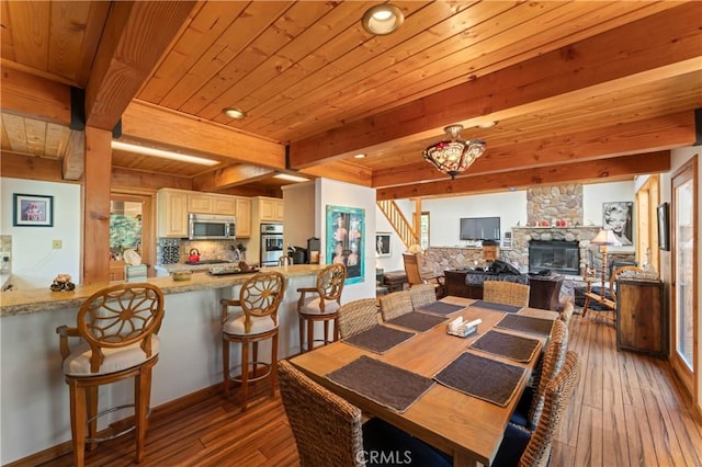 dining area featuring wood ceiling, a stone fireplace, light hardwood / wood-style floors, and beam ceiling