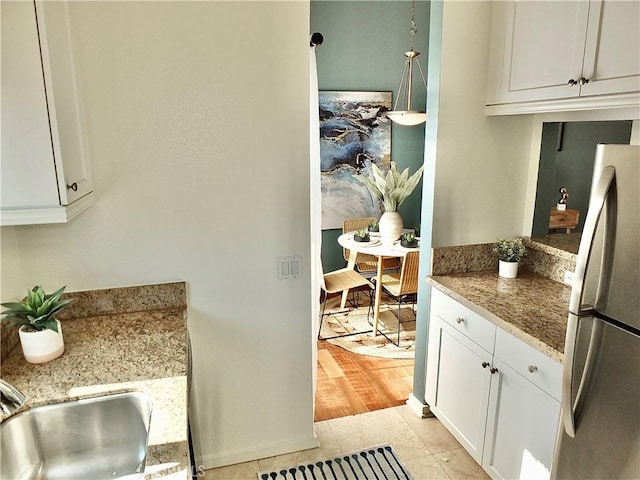 kitchen with light stone countertops, stainless steel fridge, pendant lighting, light hardwood / wood-style floors, and white cabinetry