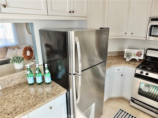 kitchen with light tile patterned floors, white cabinetry, light stone counters, and appliances with stainless steel finishes