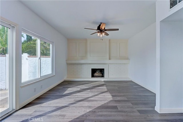 unfurnished living room with a brick fireplace, dark hardwood / wood-style floors, and ceiling fan