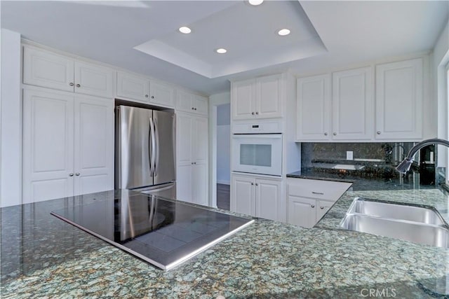 kitchen with black electric stovetop, a raised ceiling, sink, stainless steel refrigerator, and white oven